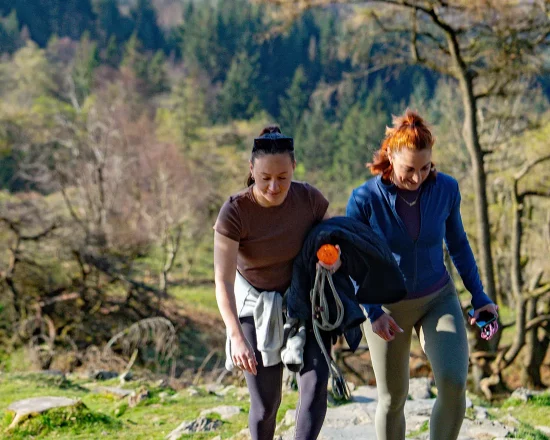 Two women walking up a rocky trail, surrounded by greenery in the Lakeland fells