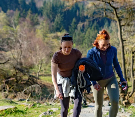 Two women walking up a rocky trail, surrounded by greenery in the Lakeland fells