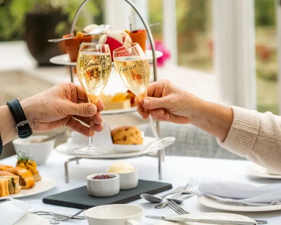Afternoon tea in conservatory setting showing finger food as a couple raise champagne glasses