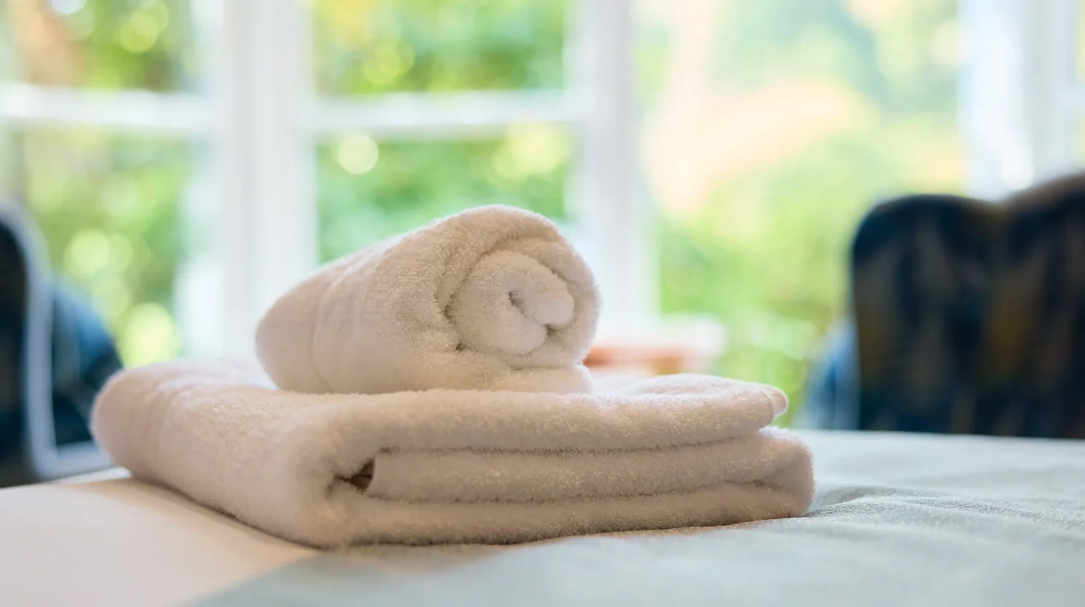 Fresh rolled up towels in bright room with nature seen in the windows behind