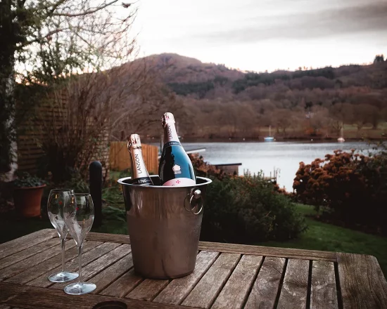 Champagne bottles chilled in a cooler with glasses on an outdoor table with lake view in background