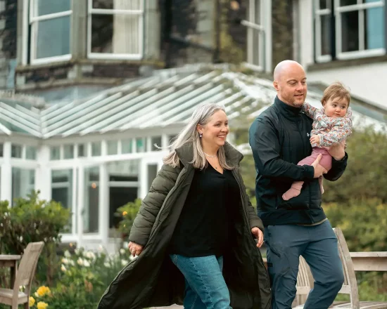Mum walking with Dad carrying their small child, in the garden at Lakeside Hotel
