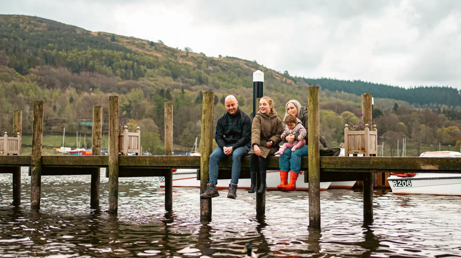 A family sat together dangling their feet off a lake jetty