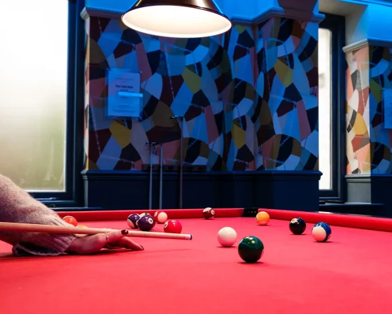 View from one end of a red pool table with someone taking aim for their next shot
