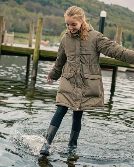 A girl kicking the water on the edge of lake Windermere wearing wellington boots