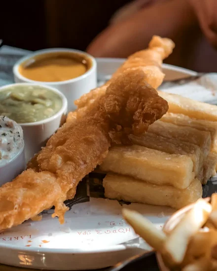 Battered fish and chunky chips on a plate with condiments
