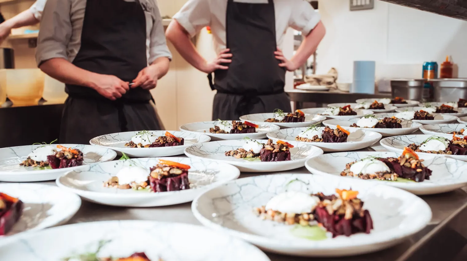 2 chefs stand proudly next to many vegetarian dishes they have prepared