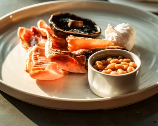 Full English breakfast plate with bacon, poached egg, mushroom and baked beans