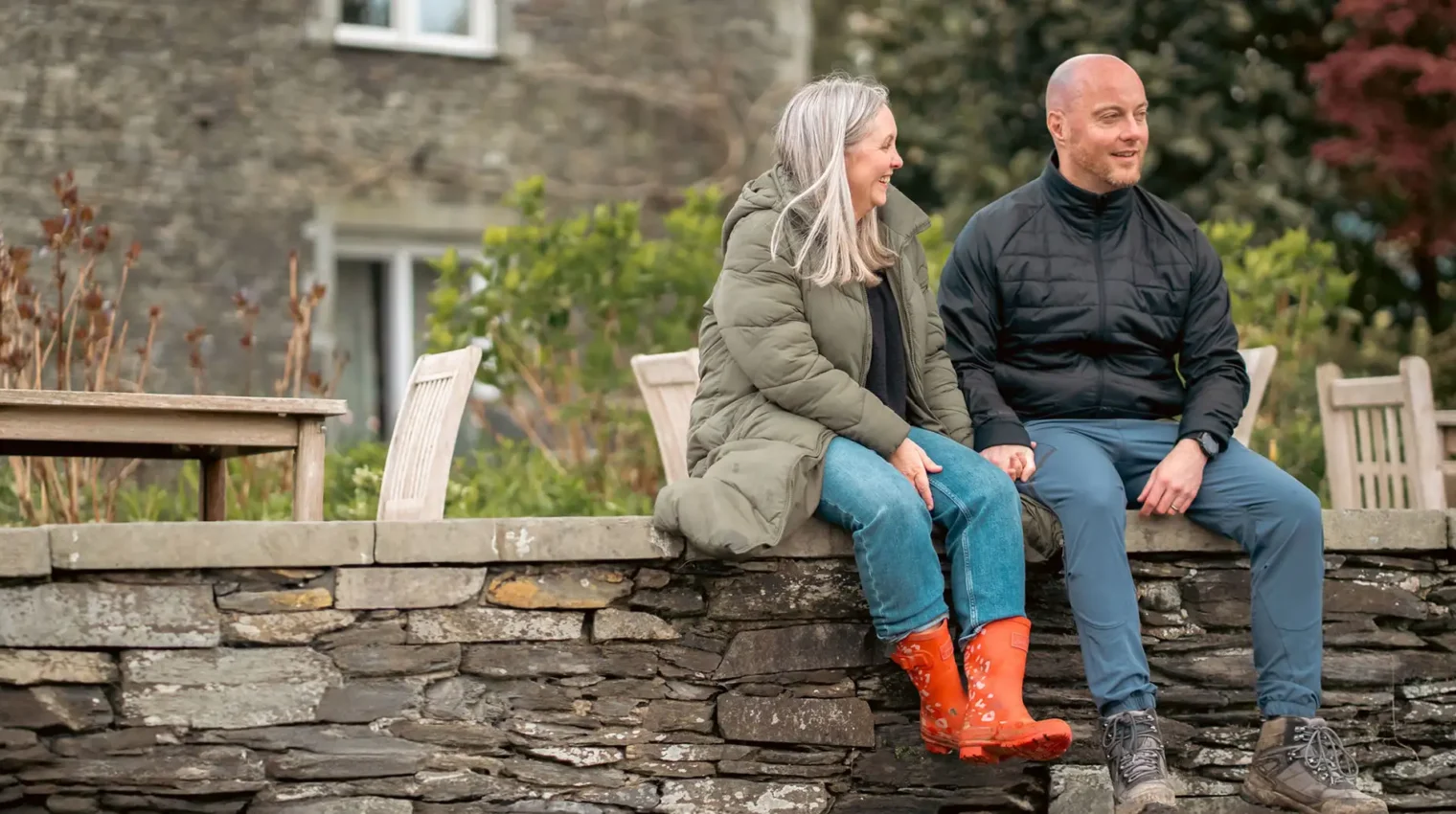 Couple dressed in outdoor gear sat on the wall in the Lakeside Hotel garden