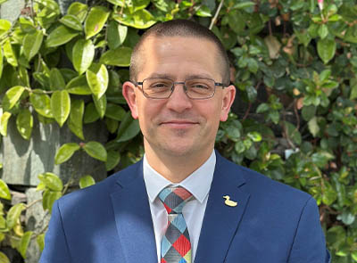 Head and shoulders of Lakeside Hotel team member with leafy background