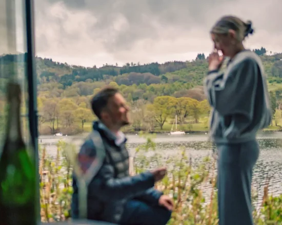A man proposes to his partner out of focus, with a view of Lake Windermere in focus in the background
